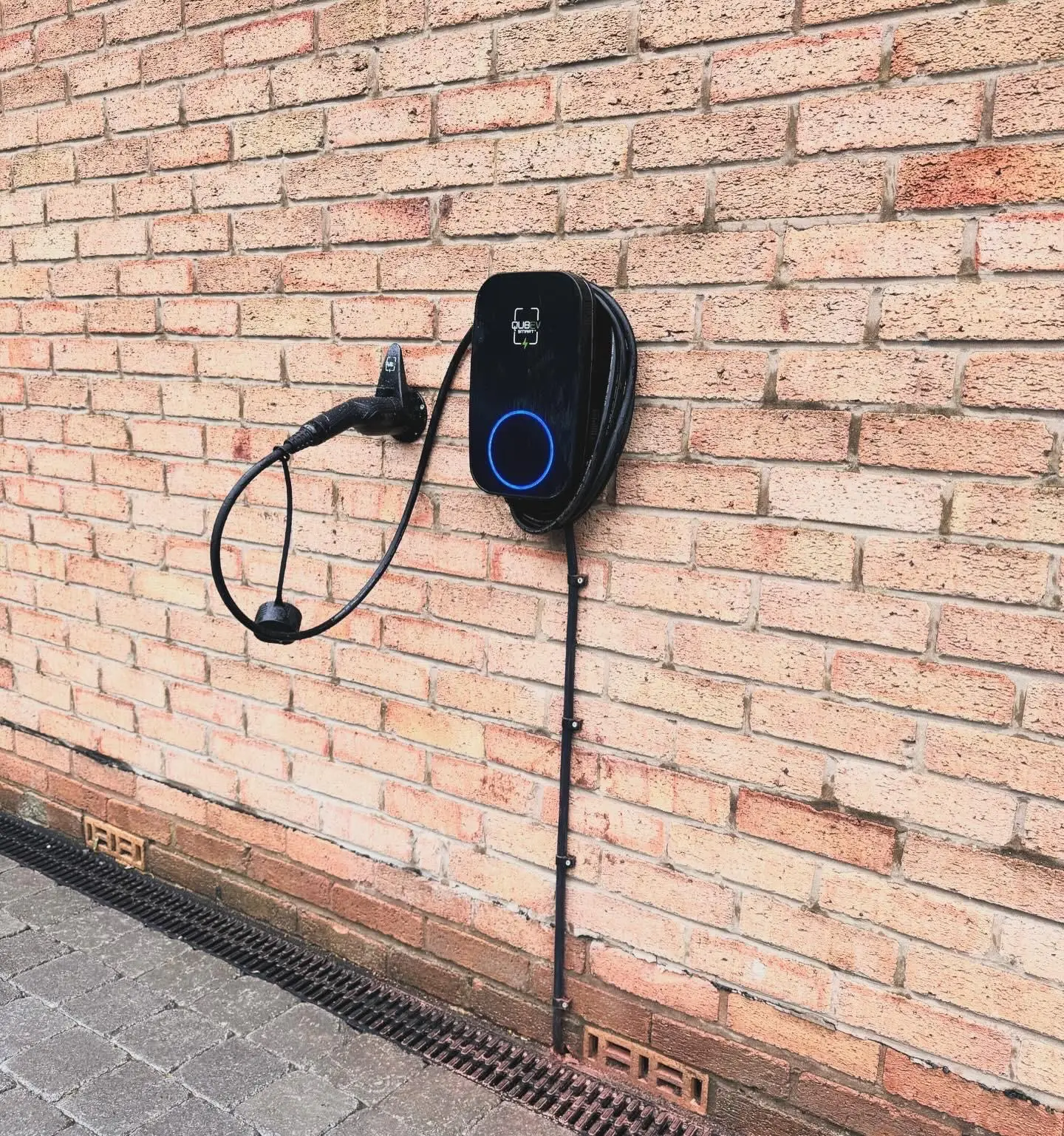 A black EV charger on a brick wall with its cable wrapped around the unit and the connector parked in a wall holster beside it.