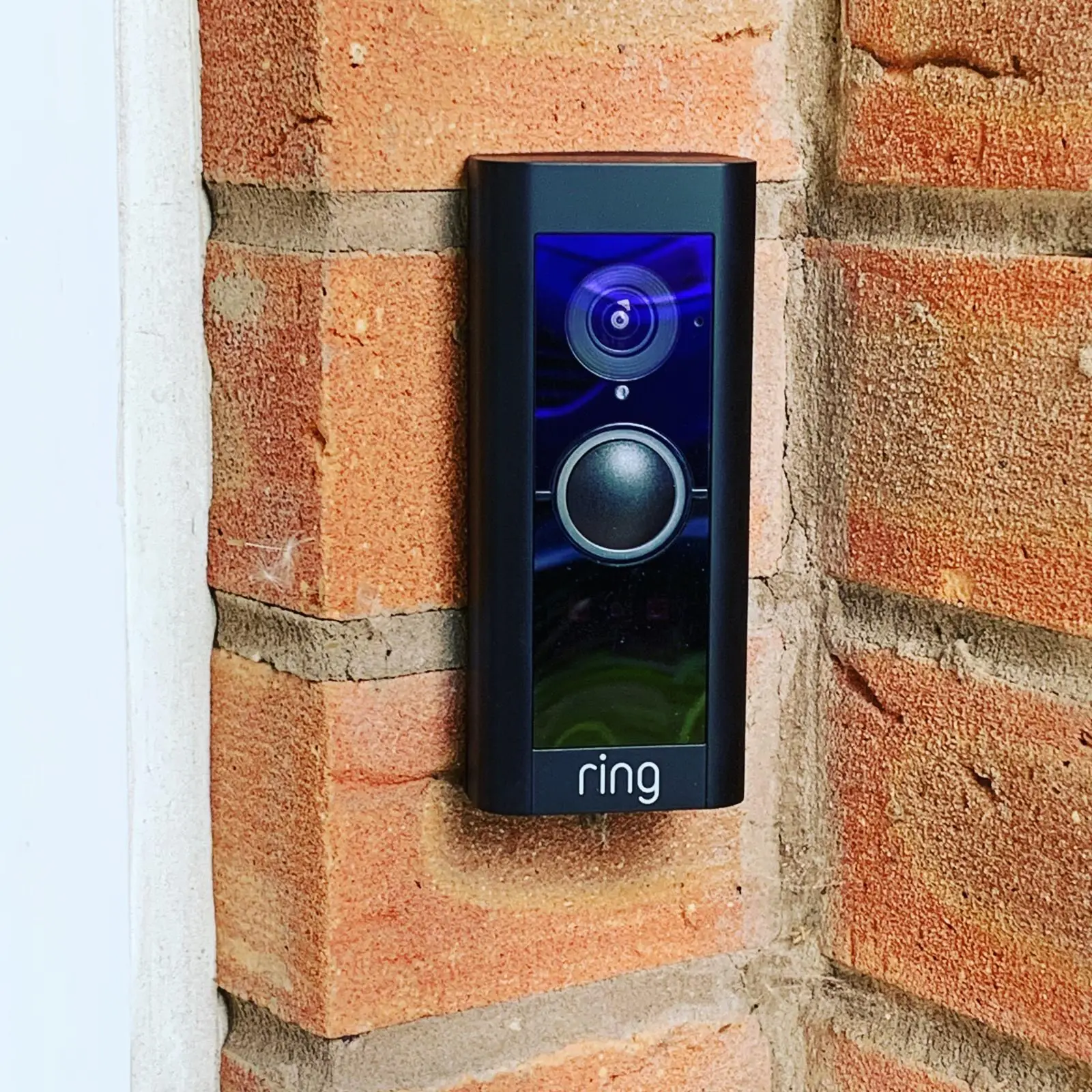 A black Ring video doorbell fitted to a brick door reveal.