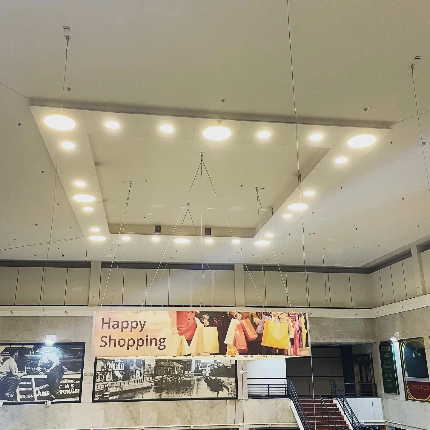 Round LED downlights in two sizes set into a suspended ceiling raft above a shopping centre atrium.