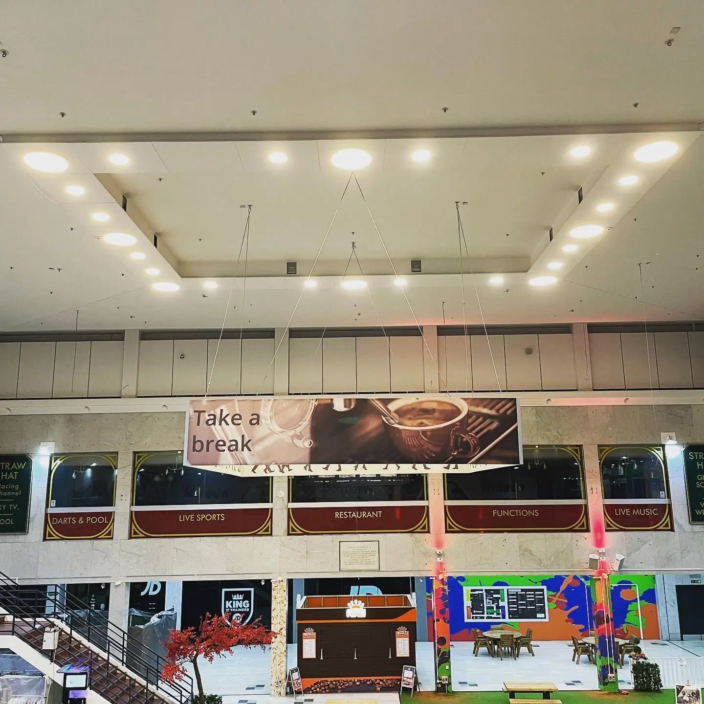 A suspended ceiling raft of round LED downlights, seen straight on from across a shopping centre atrium.