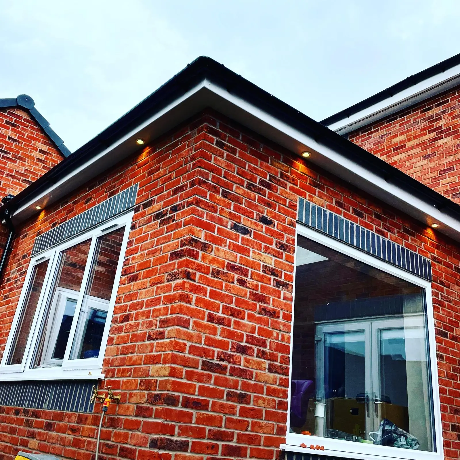 Soffit downlights fitted under the white soffit around the corner of a red brick extension.