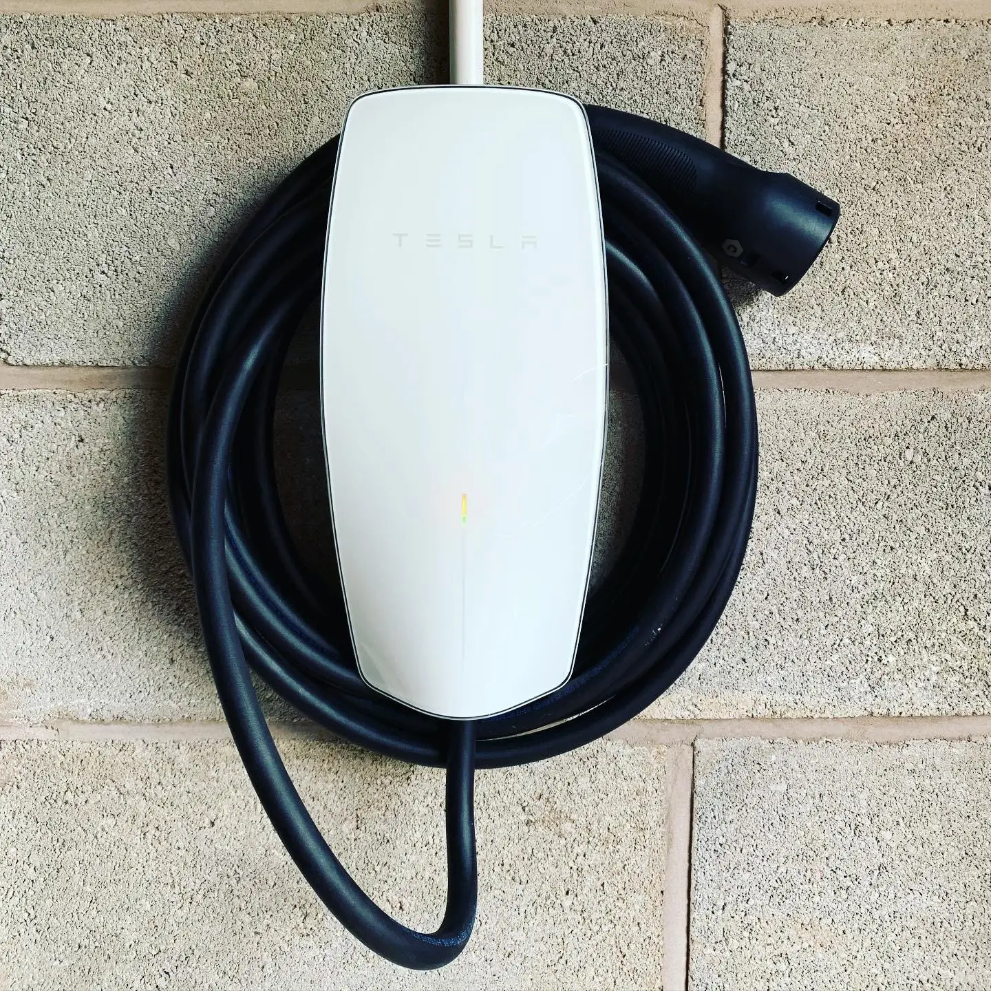 Close-up of a white Tesla wall connector with its cable coiled round the unit and the supply entering in white conduit from above.