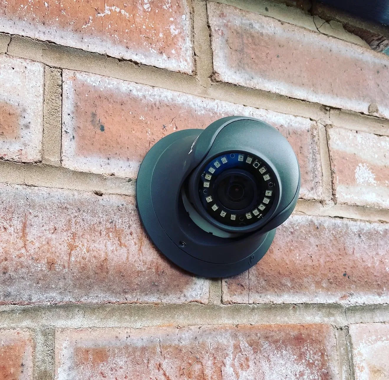 A dark grey CCTV camera with an infra-red LED ring, mounted on a brick wall.