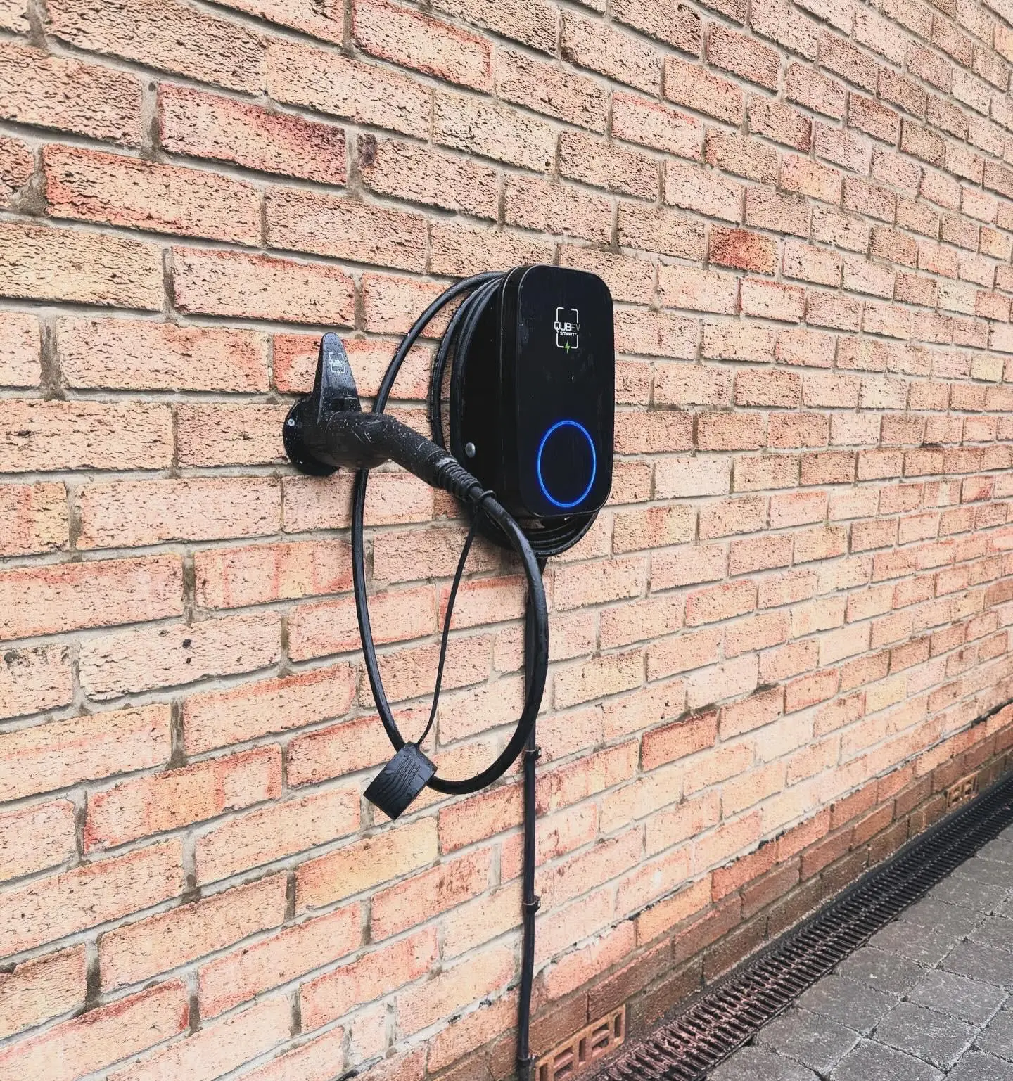 The same EV charger seen from the side, its cable looped round the unit and the supply in black conduit running down the wall.