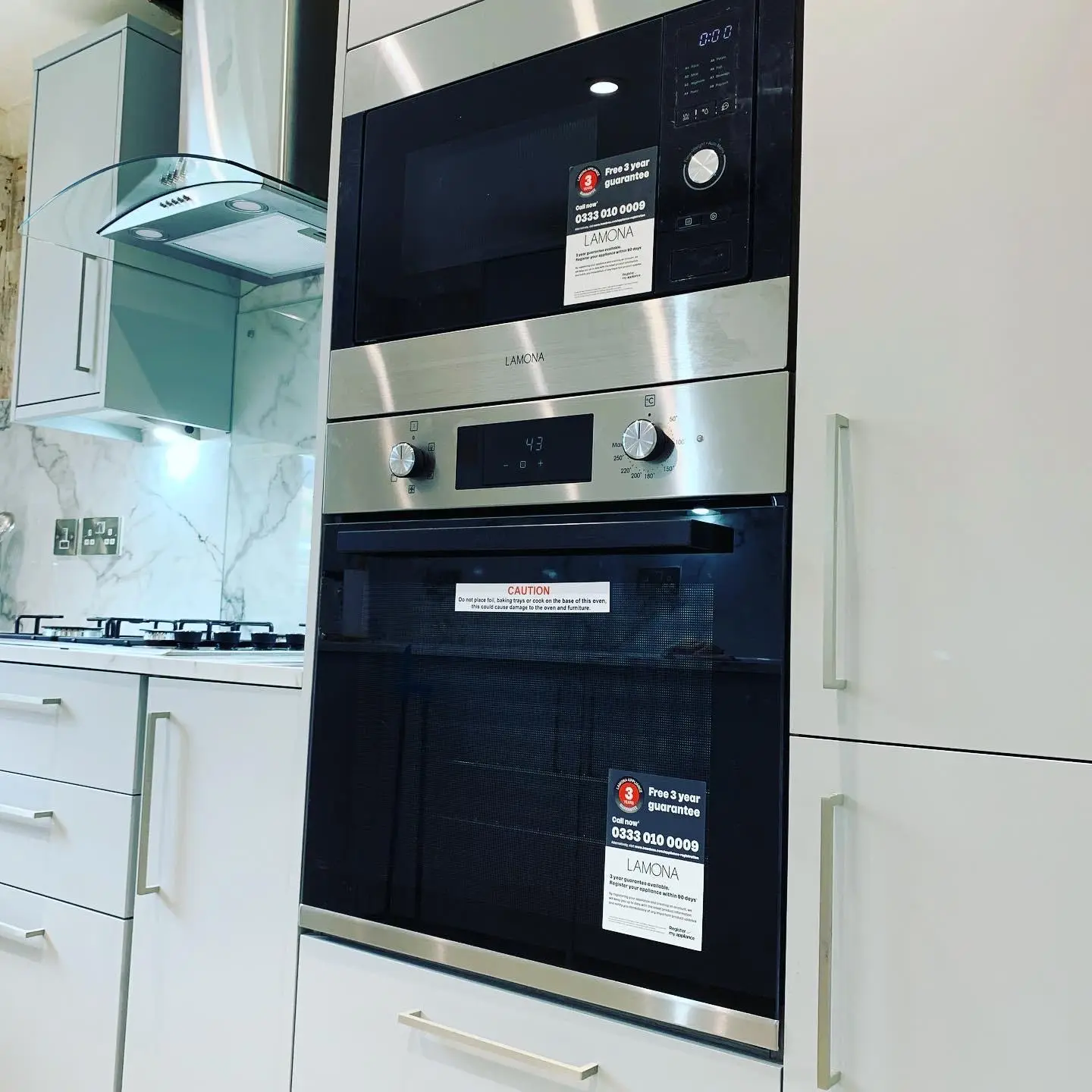A built-in oven and microwave stacked in a tall housing, with a glass chimney extractor over the gas hob and a double socket on the splashback.