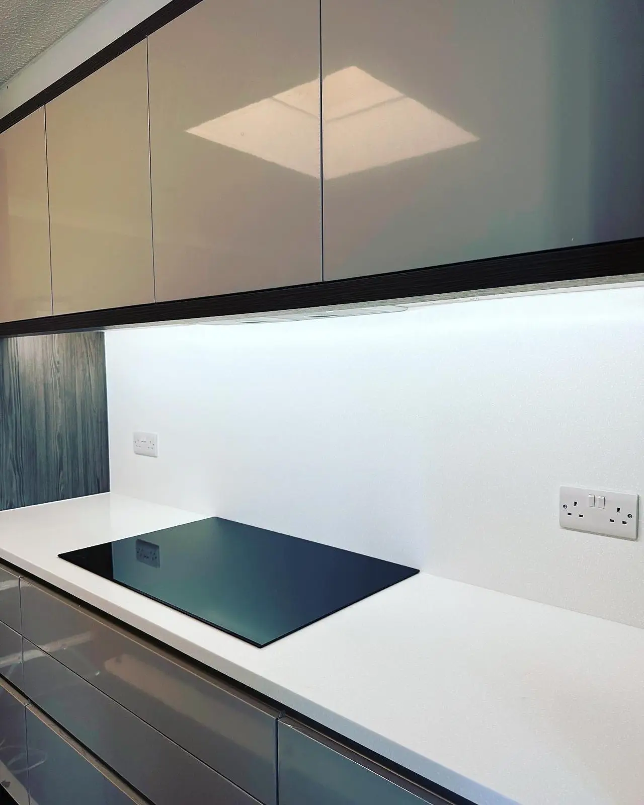 Bright LED under-unit lighting on a white splashback above an induction hob, with a white double socket either side.
