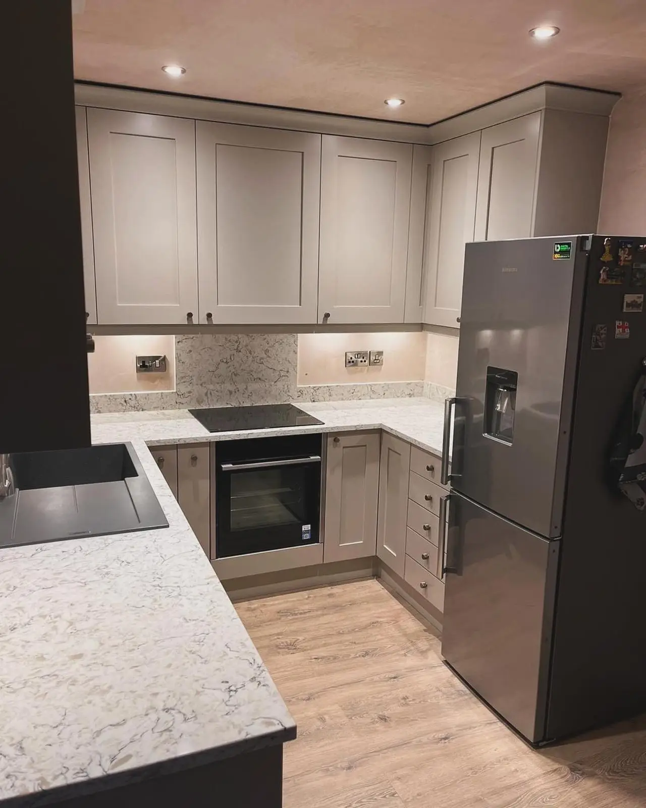 A grey shaker kitchen with LED downlights, under-unit lighting and brushed chrome sockets on the splashback, around a built-under oven and induction hob.