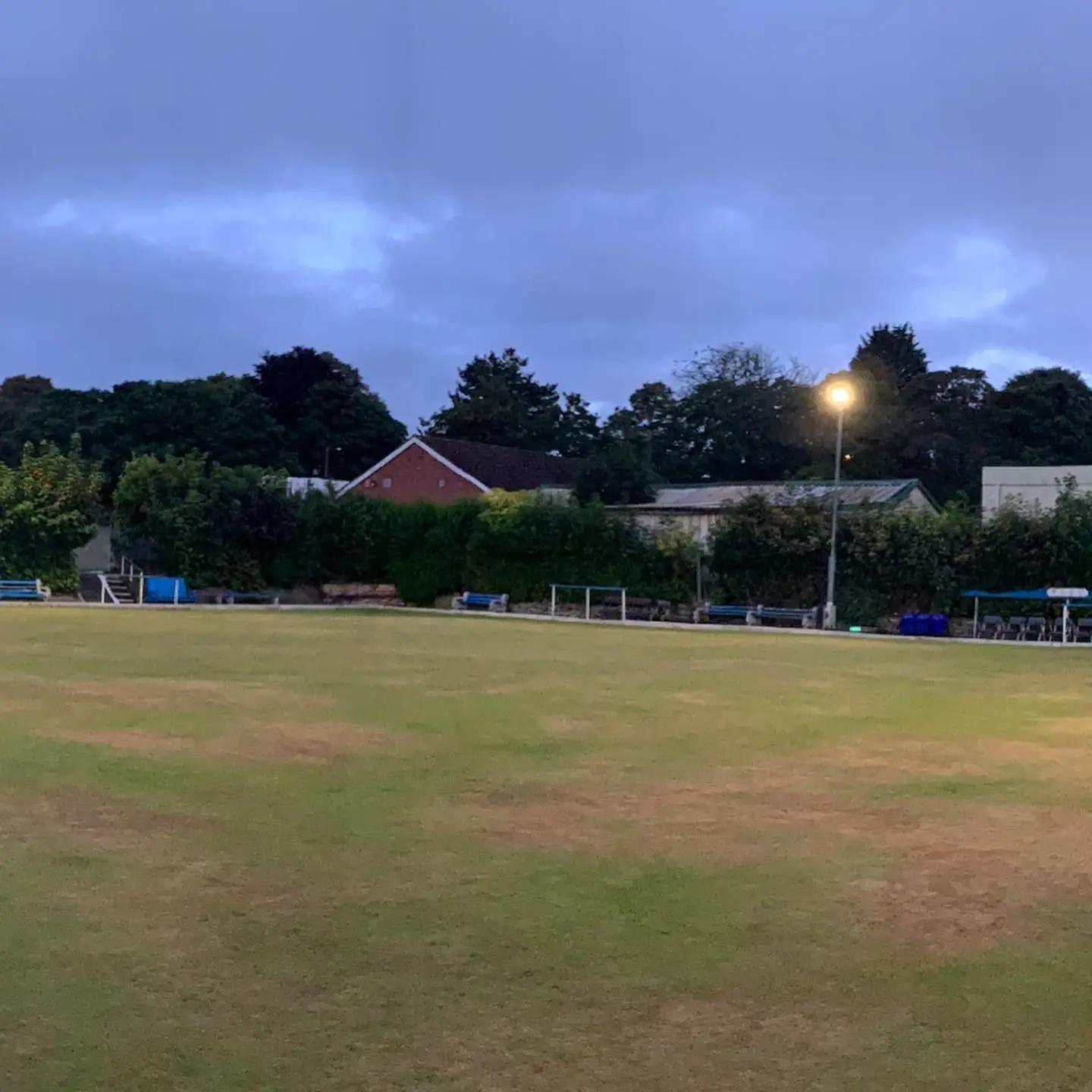 A floodlight on a column lit at dusk across the far side of a bowling green.