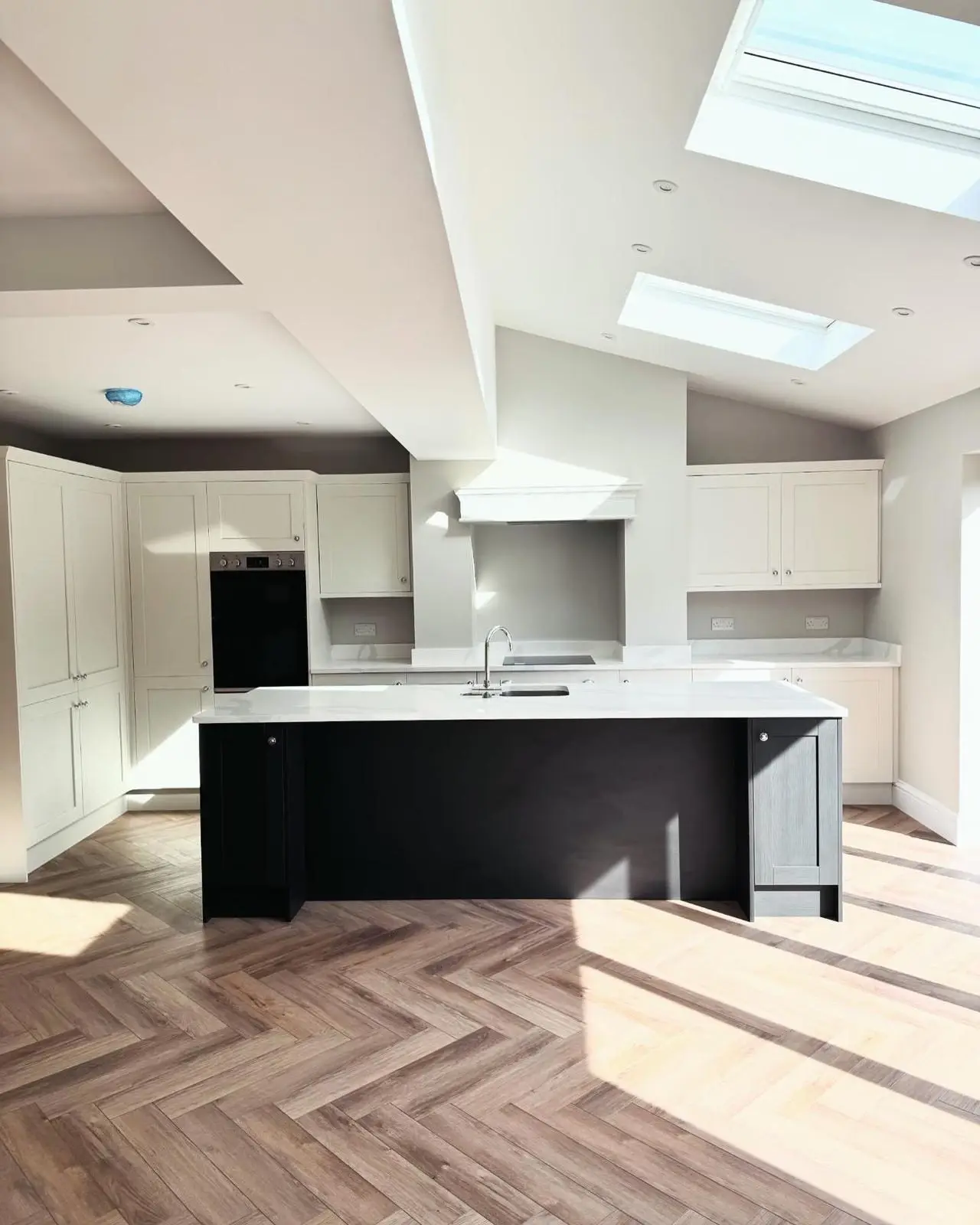 A kitchen extension with recessed downlights across the vaulted and flat ceilings, double sockets on the splashback, a built-in double oven and an induction hob.