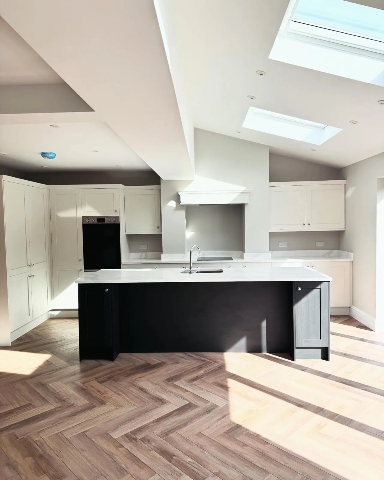 A kitchen extension with recessed downlights across the vaulted and flat ceilings, double sockets on the splashback, a built-in double oven and an induction hob.
