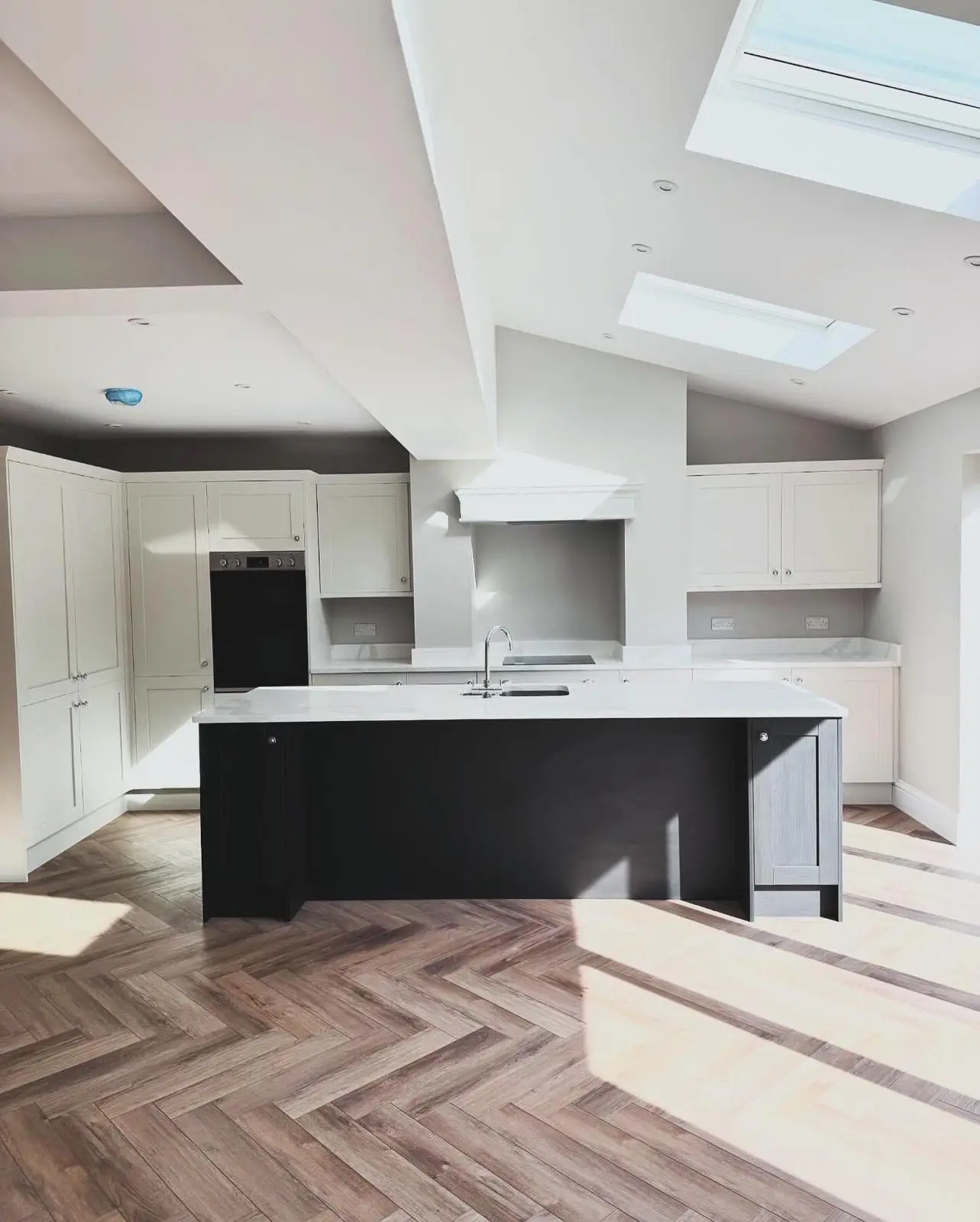 Straight-on view of a kitchen extension with recessed downlights across the ceiling, double sockets along the splashback and a built-in double oven.