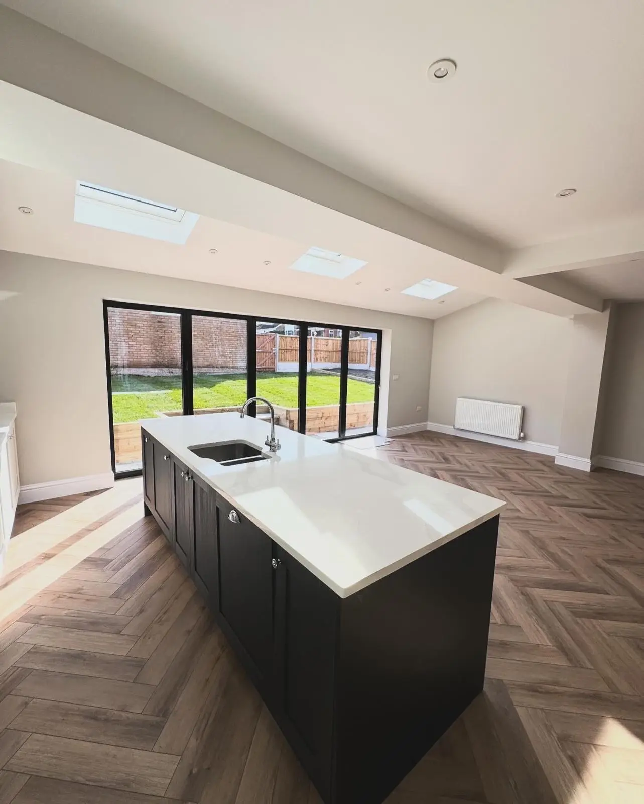 An open-plan kitchen extension with recessed downlights across the ceiling between three rooflights, a light switch by the bifold doors and a socket on the far wall.