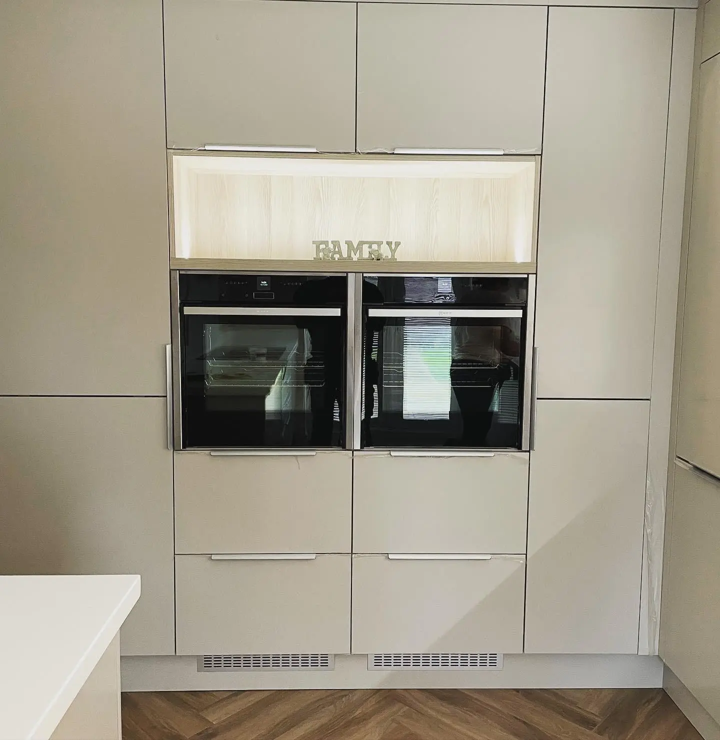 Two built-in ovens side by side in tall handleless units, with an open shelf above lit by LED tape.