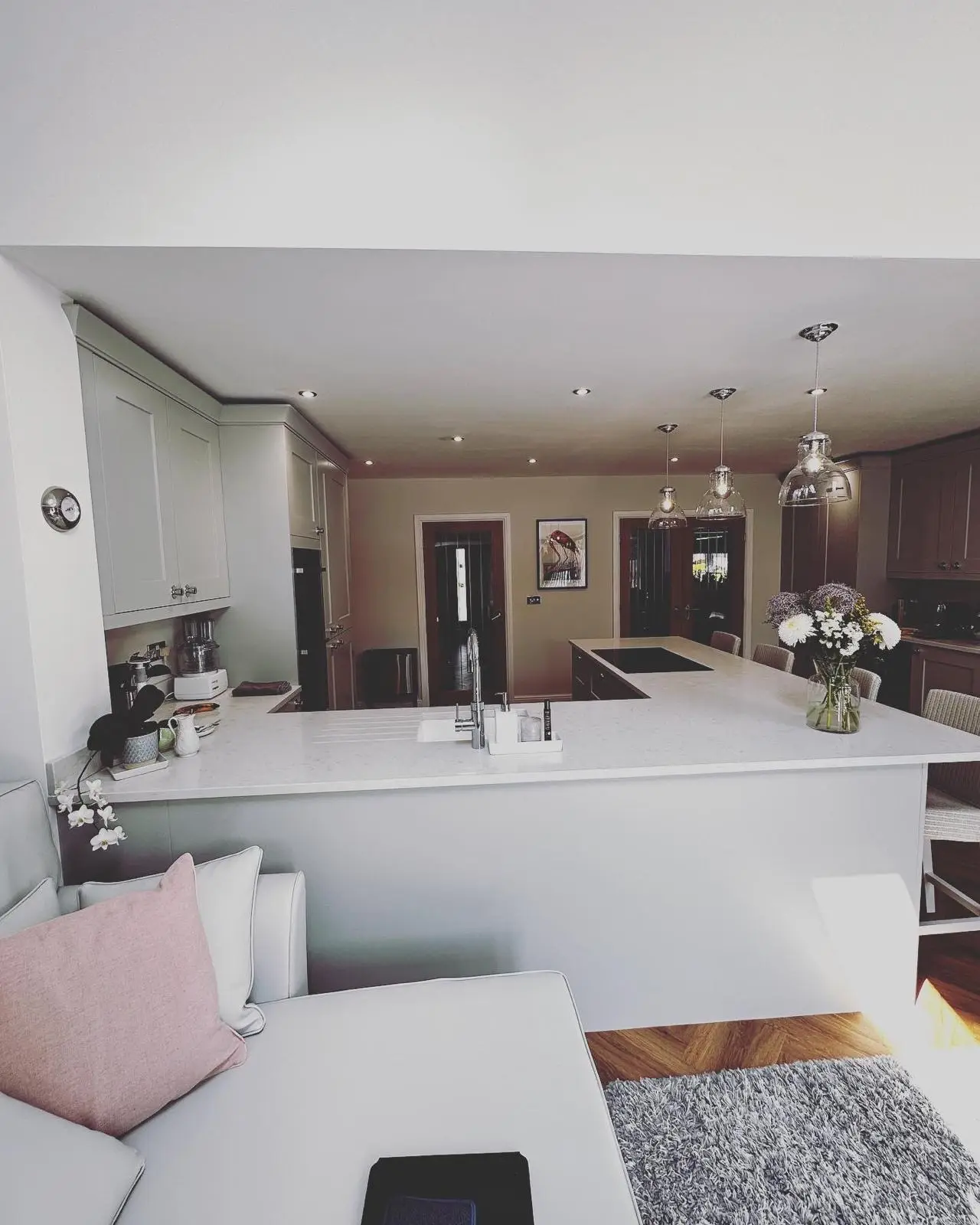 Three glass pendants and LED downlights over a kitchen peninsula, seen from the sofa in an open-plan living area.