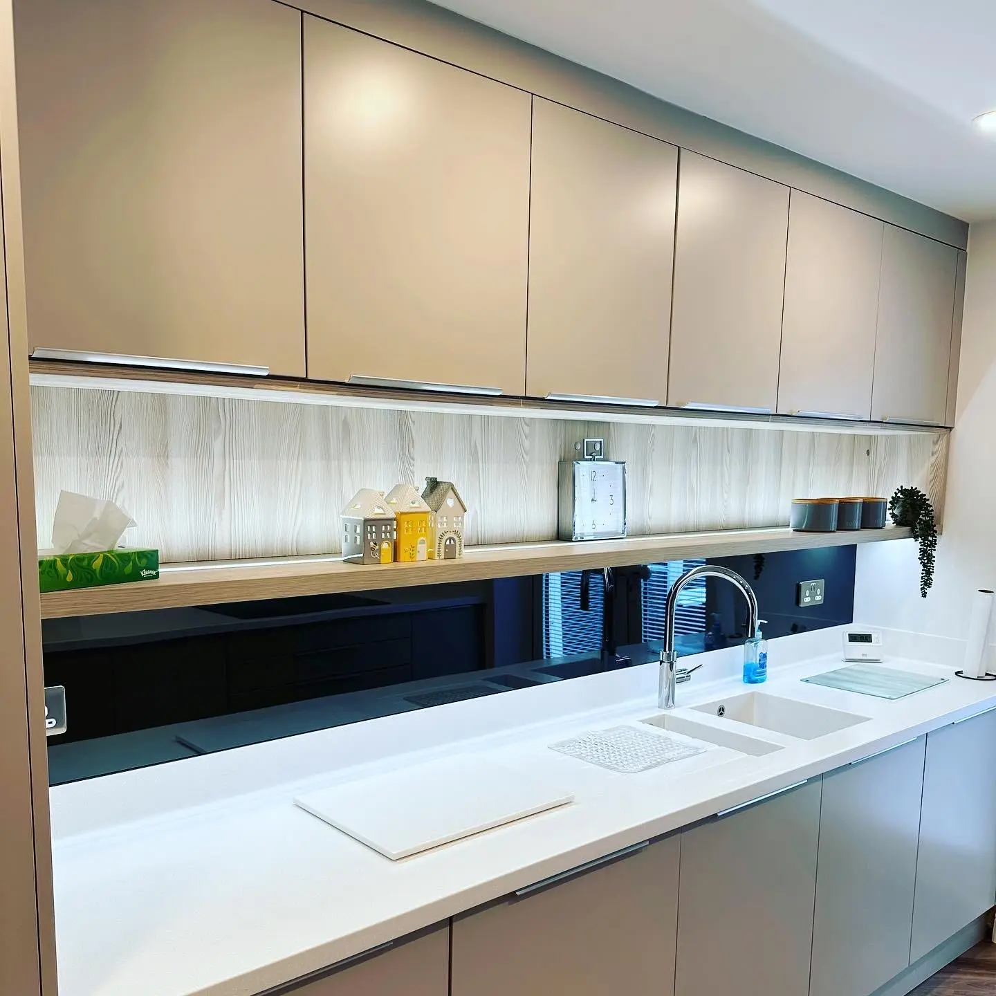 A long handleless kitchen run with LED tape under the wall units and along a long open shelf, and brushed chrome double sockets at either end.