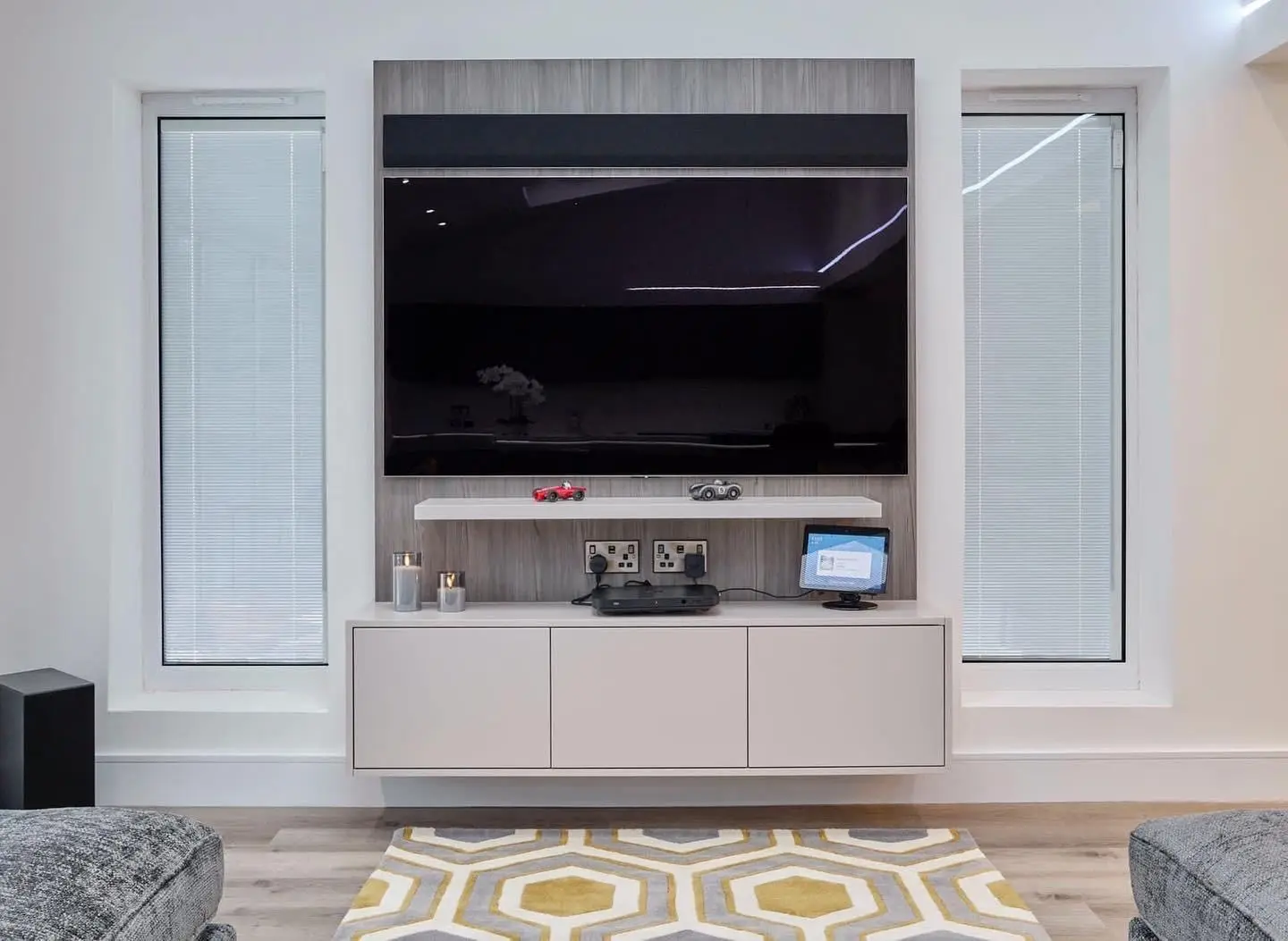 A media wall with a TV and soundbar on a timber-effect panel, and two brushed double sockets with USB ports set below the floating shelf.