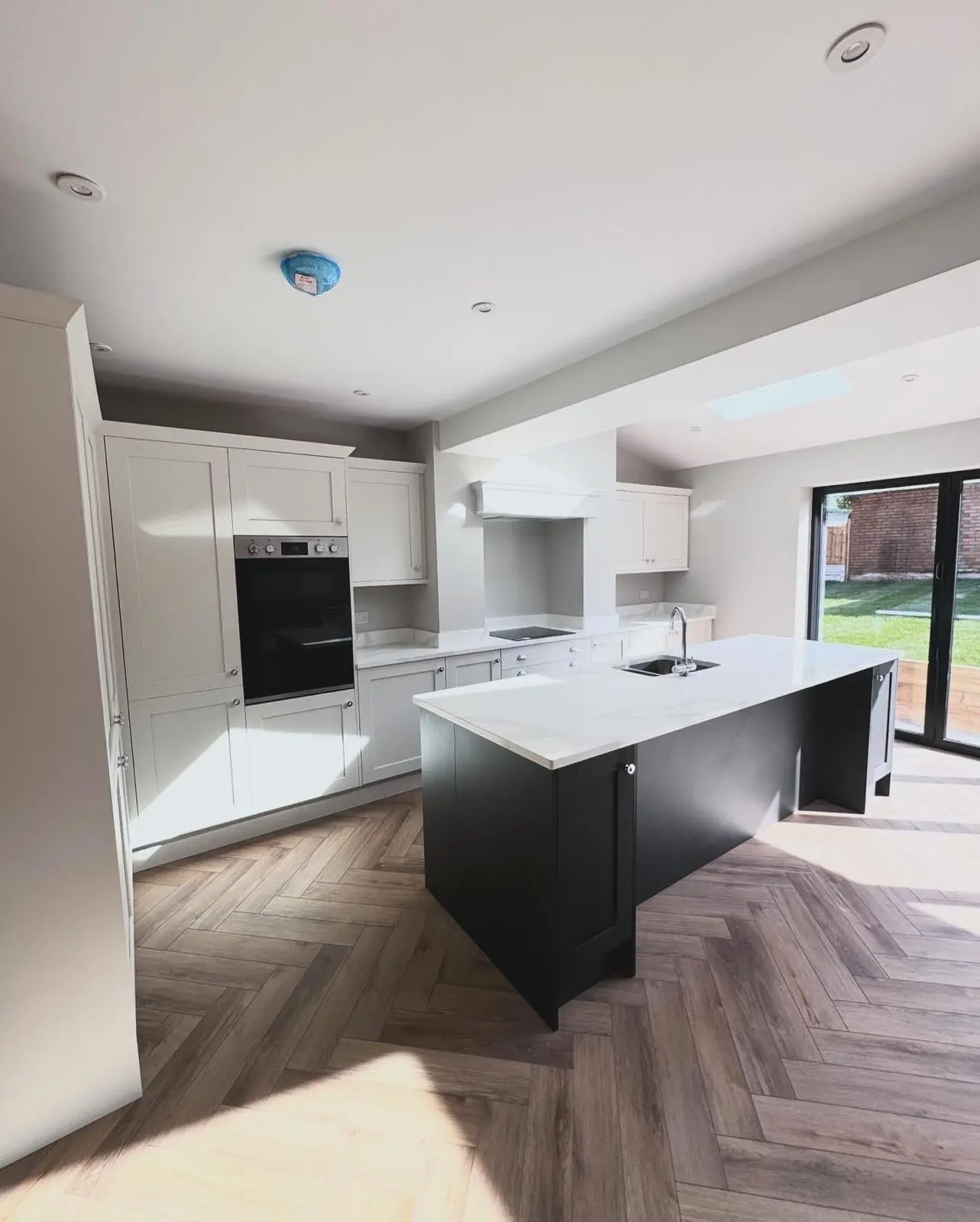 A kitchen extension looking towards the bifold doors, with recessed downlights, a built-in double oven, an induction hob and double sockets on the splashback.