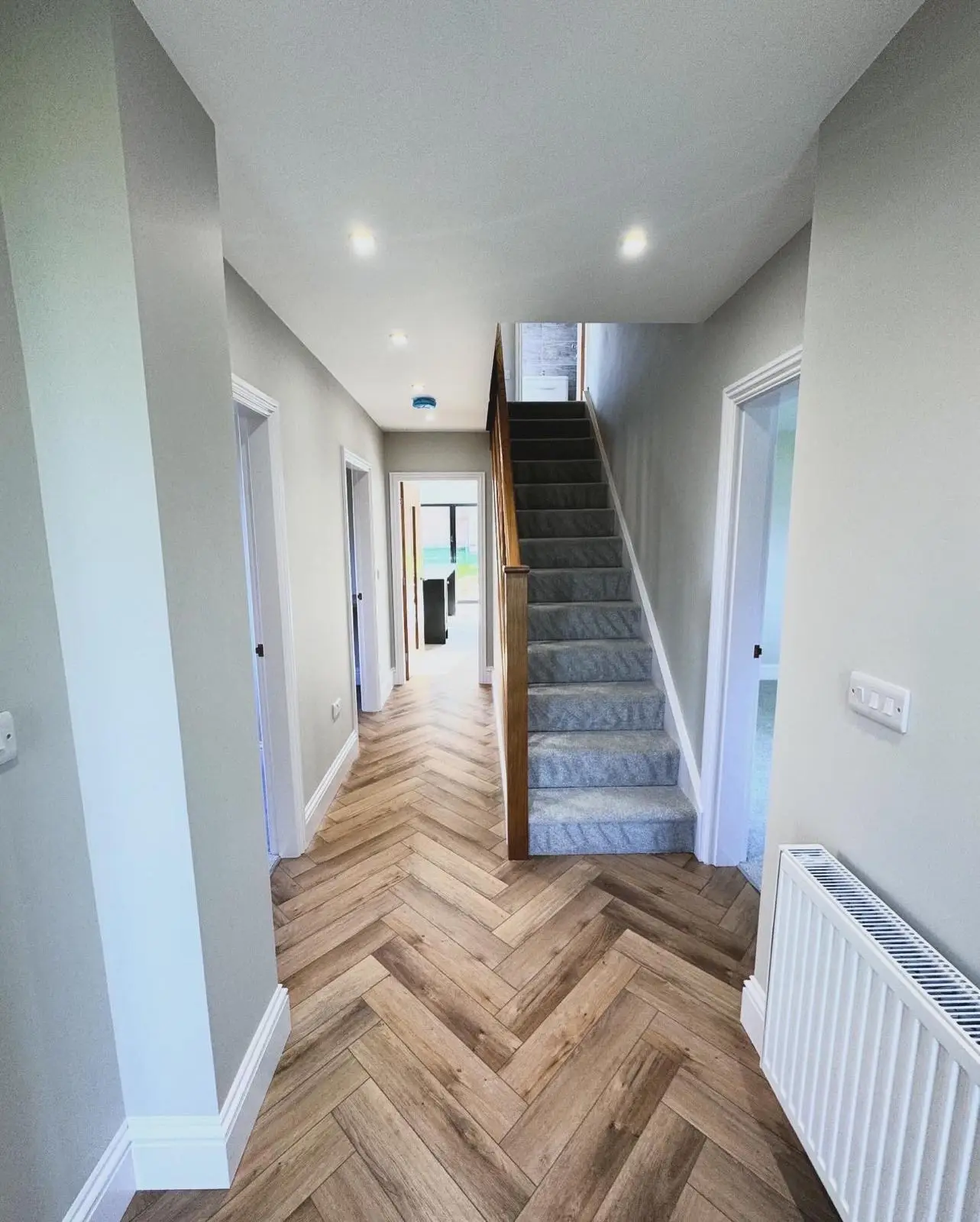 A hallway with LED downlights along the ceiling, a white three-gang light switch by a doorway and a socket low on the wall.