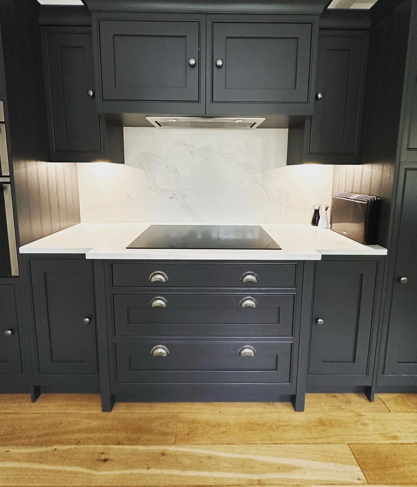 An extractor built in under the wall units above an induction hob, with under-unit lighting either side on a marble-effect splashback.